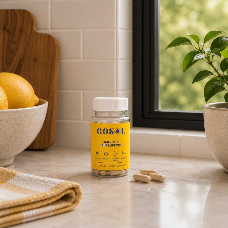 A bottle of GOSUL Daily Sun Skin Support dietary supplements sits on a marble kitchen counter next to a window, with lemon slices in a bowl and a potted plant in the background.