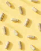 Multiple beige capsules arranged diagonally on a solid pale yellow background with soft shadows.