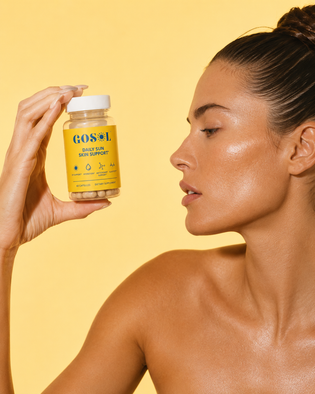 A woman in profile holds up a bottle of GOSOLs Daily Sun Skin Support against a solid yellow background.