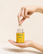 A hand holds an open clear supplement bottle with a bright yellow label reading GOSOL Daily Sun Skin Support, while another hand drops two beige capsules above it. The background is a clean, warm off-white studio setting.