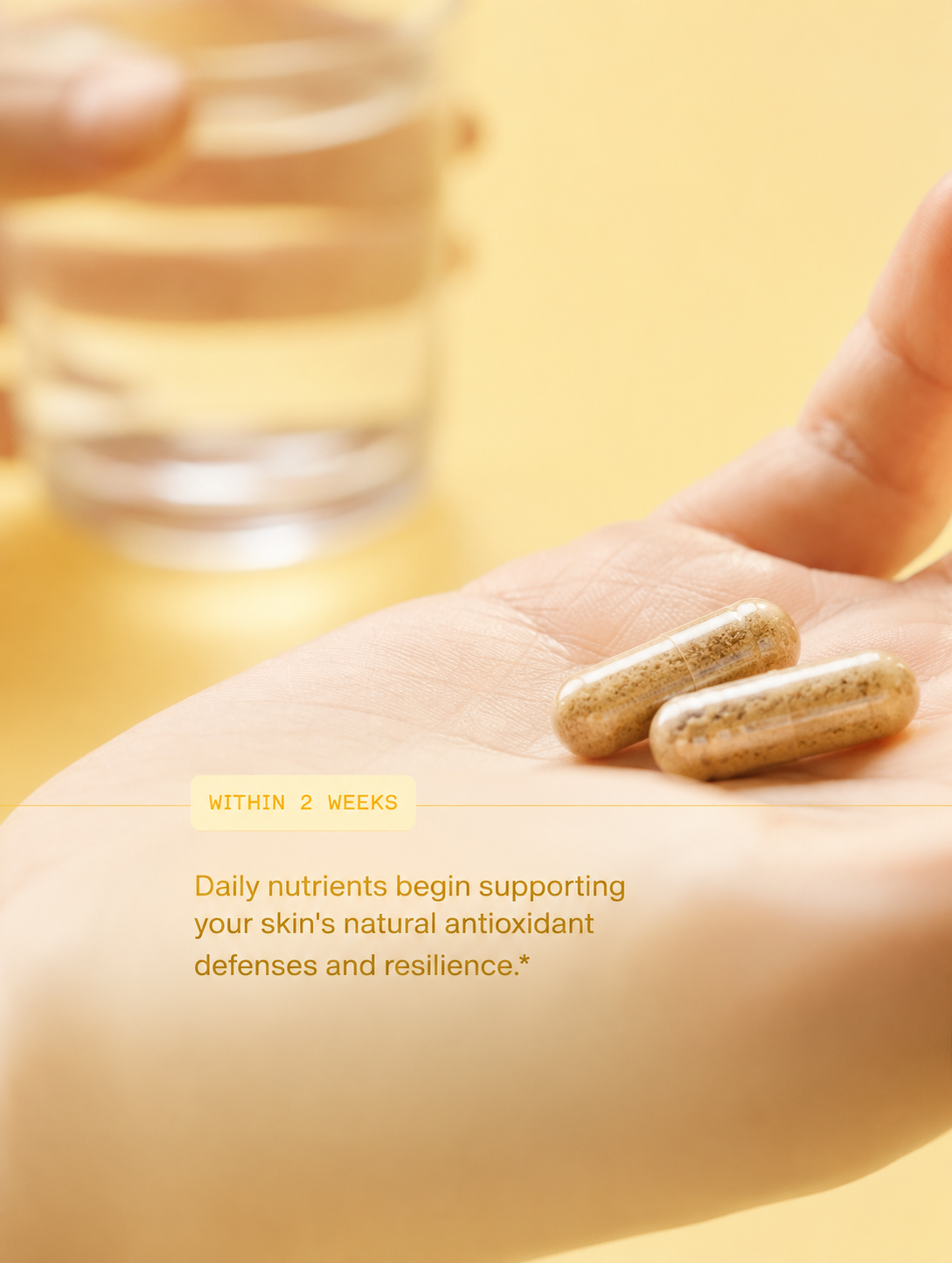 Two beige dietary supplement capsules resting on an open palm, with a blurred glass of water in the background and text overlay reading 'WITHIN 2 WEEKS' and 'Daily nutrients begin supporting your skin's natural antioxidant defenses and resilience.'.