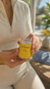 Woman puring two GoSol capsules from the bottle into her hand. Woman is wearing cream athleisure attire. Background is sunny blurred out background.