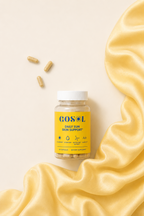 A bottle of GOSOL Daily Sun Skin Support dietary supplement capsules, styled on a cream background with draped yellow satin fabric and three loose capsules.